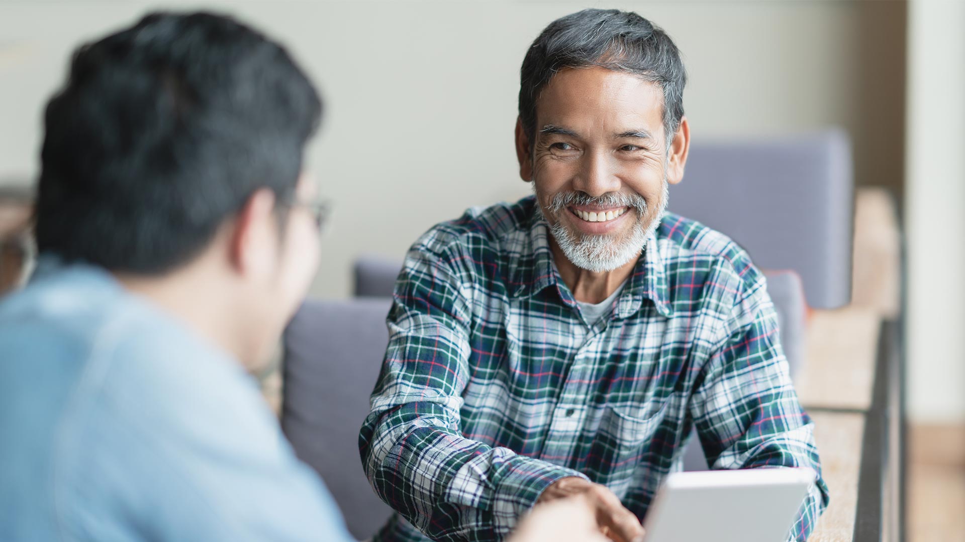 Two men sit smiling at each other reviewing documentation to represent the ndis audit process